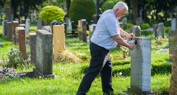 Ein Friedhofsaufseher testet auf dem Pragfriedhof in Stuttgart die Standfestigkeit eines Grabsteins.