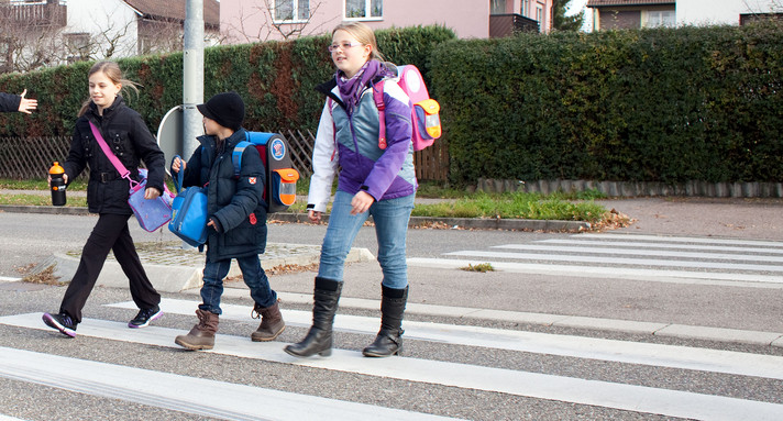 Schülerlotse geht mit Schulkindern über Zebrastreifen