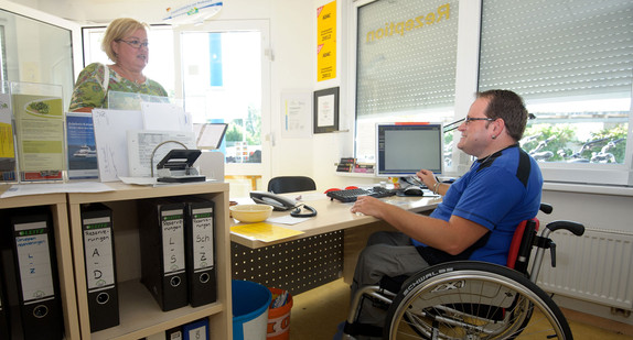 Ein Mann im Rollstuhl arbeitet an der Rezeption eines Campingplatzes. (Foto: © dpa)