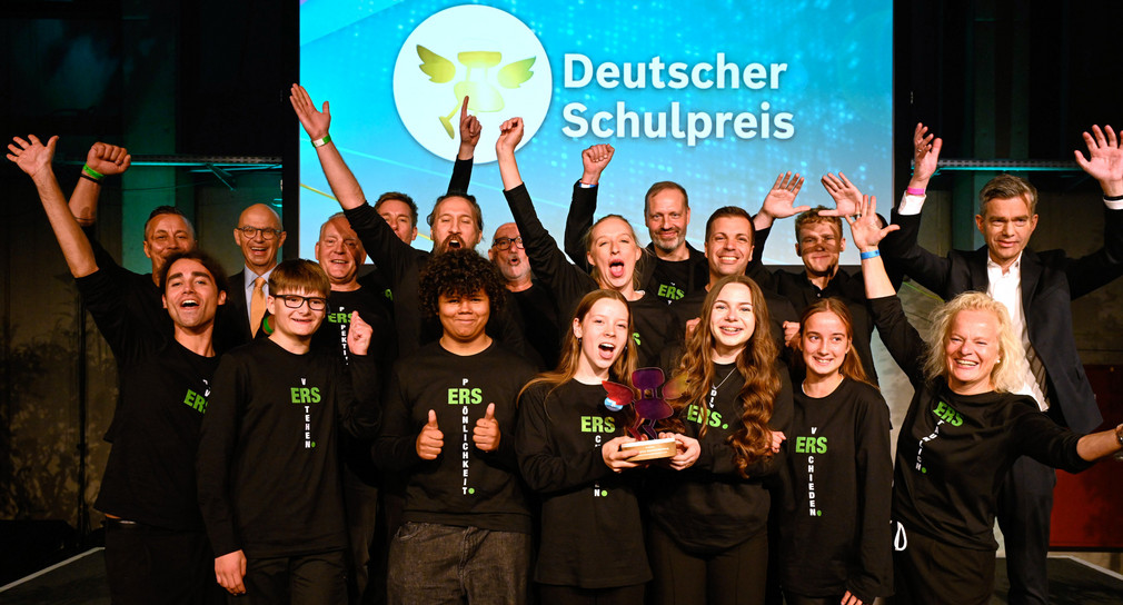 Eine Grupppe von Jungen und Mädchensteht auf einem Podium und streckt die Fäuste in die Luft. 