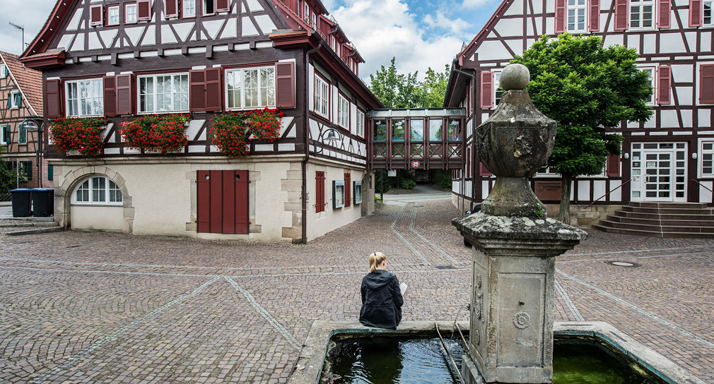 Symbolbild: Eine Frau sitzt an einem Dorfbrunnen. (Foto: © dpa)