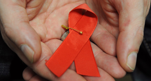 Ein mit dem HI-Virus infizierter Mann hält eine rote Schleife als Symbol der Solidarität mit HIV-Positiven und Aids-Kranken.
