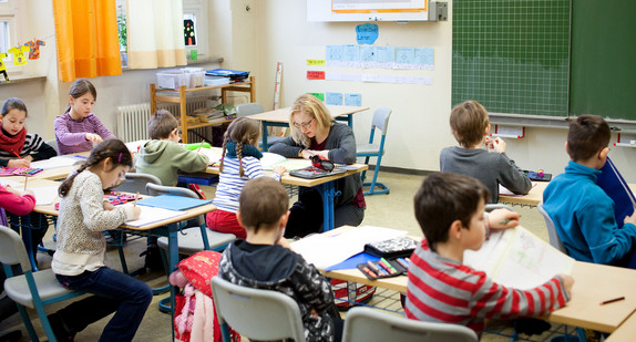 Eine Grundschullehrerin erklärt Schülerinnen und Schülern Aufgaben.