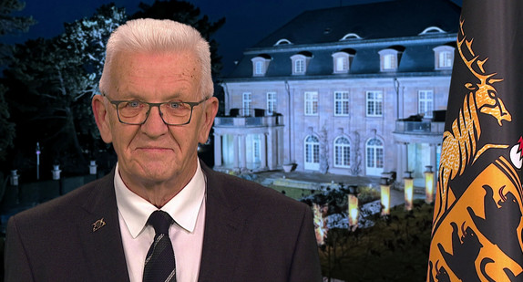 Ministerpräsident Winfried Kretschmann bei seiner Ansprache zum Jahreswechsel 2025/2026, im Hintergrund die Villa Reitzenstein, rechts im Bild die Baden-Württemberg-Fahne.