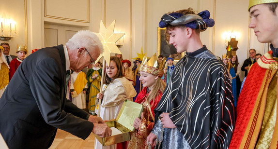 Ministerpräsident Winfried Kretschmann (links) überreicht den Sternsingerinnen und Sternsingern eine Geldspende.