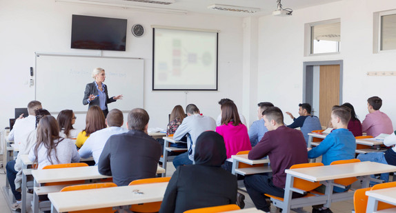 Eine Professorin steht beim Unterricht vor Studentinnen und Studenten.