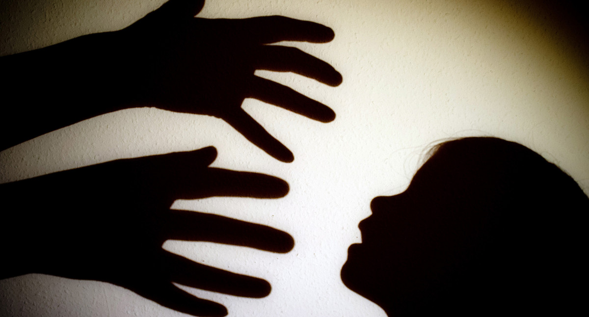 Symbolbild: Schatten von Händen einer erwachsenen Person und dem Kopf eines Kindes sind an einer Wand eines Zimmers zu sehen.