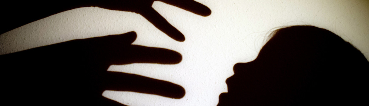 Symbolbild: Schatten von Händen einer erwachsenen Person und dem Kopf eines Kindes sind an einer Wand eines Zimmers zu sehen.