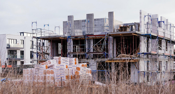 Neu gebaute Häuser stehen hinter einer noch unbebauten Fläche eines Neubaugebiets.
