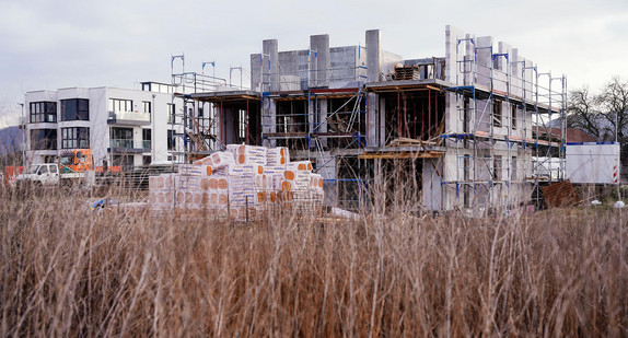 Neu gebaute Häuser stehen hinter einer noch unbebauten Fläche eines Neubaugebiets.