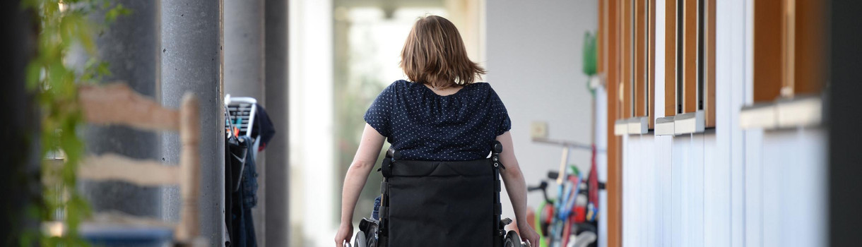 Eine Rollstuhlfahrerin fährt in einer Wohnanlage zu ihrer Wohnung. (Foto: © dpa)
