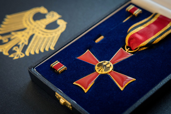 Das Verdienstkreuz am Bande des Verdienstordens der Bundesrepublik Deutschland in einer Schatuelle, darunter leigt eine Urkunde.