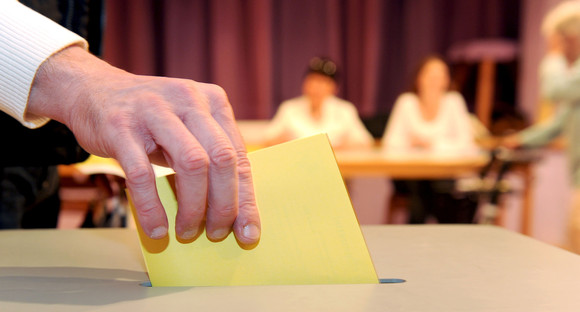 Ein Wahlzettel wird in eine Wahlurne geworfen. (Foto: © dpa)