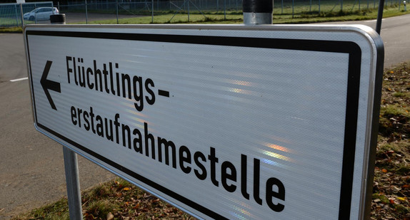 Ein Schild mit der Aufschrift „Flüchtlingserstaufnahmestelle“, im Hintergrund ein Fahrzeug an einer Einfahrt.