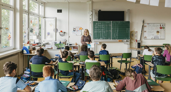 Eine Lehrerin steht in einem Klassenzimmer vor einer Schulklasse.