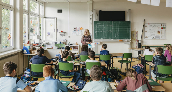 Eine Lehrerin steht in einem Klassenzimmer vor einer Schulklasse.