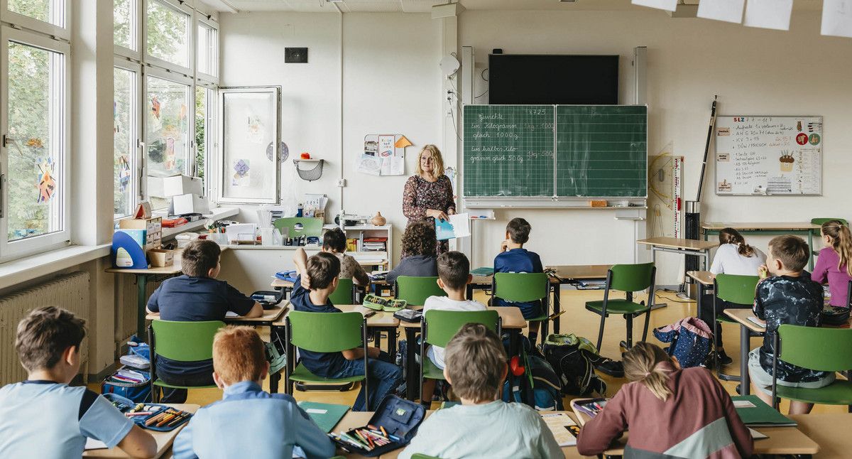Eine Lehrerin steht in einem Klassenzimmer vor einer Schulklasse.