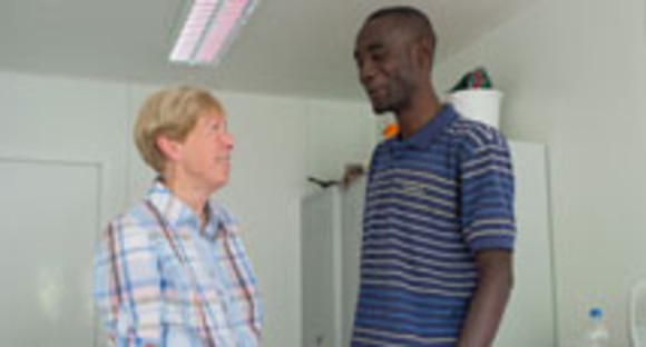 Eine ehrenamtliche Helferin spricht in Schwetzingen in einem Zimmer der Flüchtlingsunterkunft mit einem Flüchtling aus Gambia (Bild: © dpa).