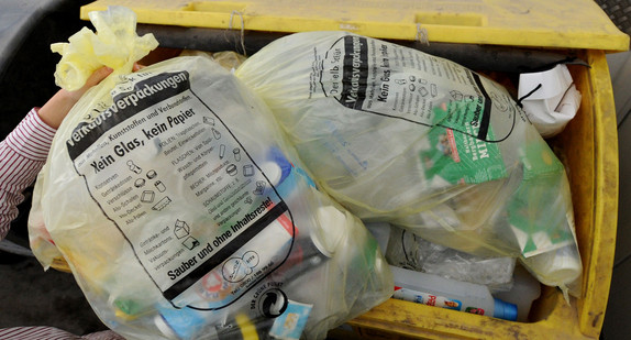 Eine Frau wirft am in einen Gelben Sack in einen gelben Abfallbehälter. (Foto: © dpa)