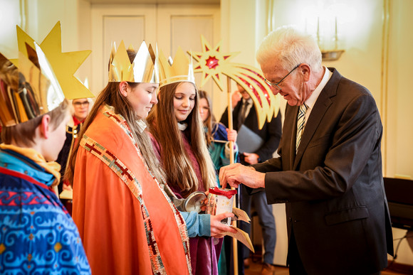 Ministerpräsident Winfried Kretschmann (rechts) überreicht den Sternsingerinnen und Sternsingern eine Geldspende.