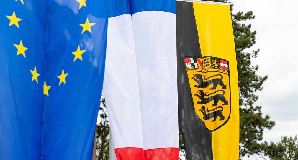 An Fahnemasten hängen die Fahne der EU, die französische Fahne und die baden-württembergische Fahne.
