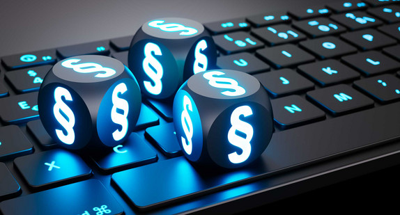 Drei leuchtende Würfel mit Paragrafen-Zeichen liegen auf einer Computer-Tastatur.