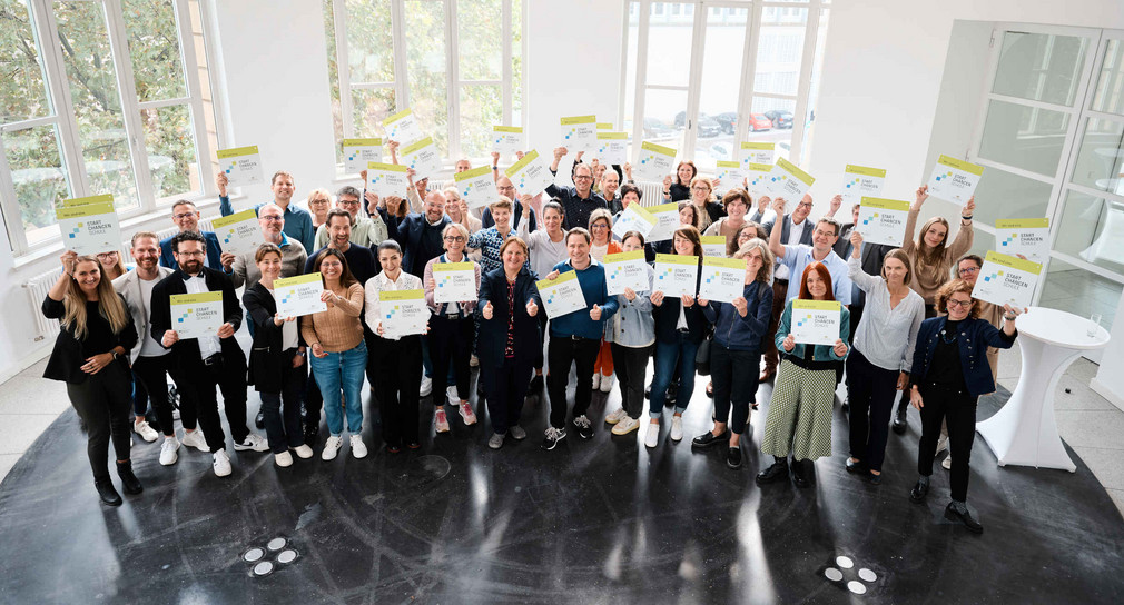 Gruppenbild von Lehrkräften, die Startchancen-Schilder in die Höhe halten, mit Kultusministerin Schopper