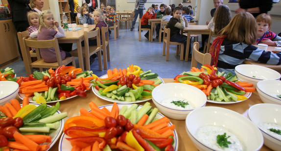 Schüler warten auf ihr Mittagessen, im Vordergrund stehen Teller mit geschnittenem Gemüse.