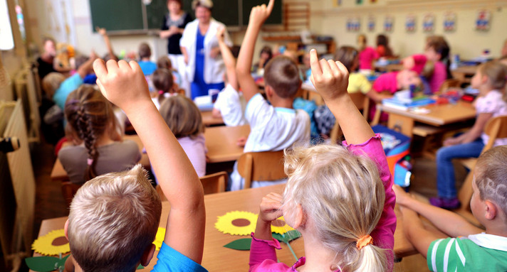 Schüler einer Grundschule melden sich im Unterricht (Bild: © dpa).