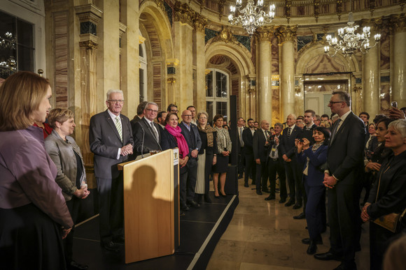 Ministerpräsident Winfried Kretschmann (Dritter von links) spricht zu den Gästen, neben ihm stehen die Mitglieder der Landesregierung.