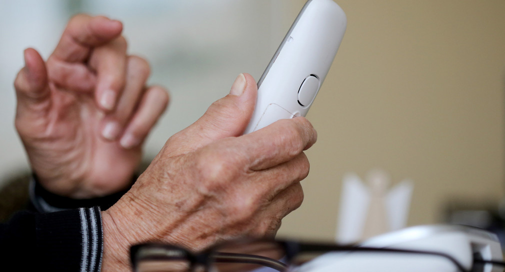 Ein älterer Mensch greift zum Telefon.