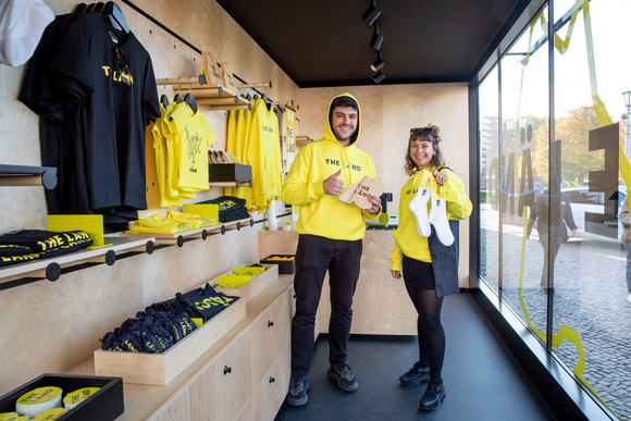 Ein Mann und eine Frau im mobilen „Fän“-Shop in Form eines umgebauten Frachtcontainers vor dem Neuen Schloss in Stuttgart