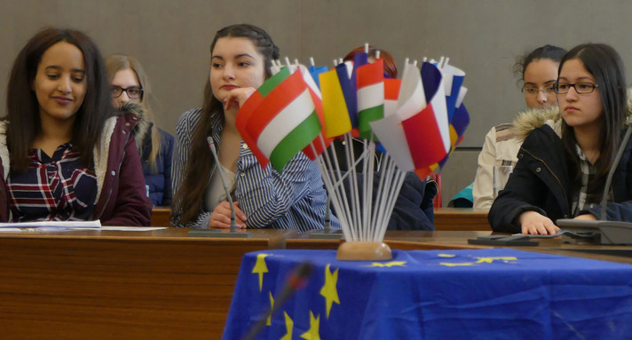 Schüler sitzen bei einem Planspiel an Tischen, im Vordergrund stehen kleine Flaggen verschiedener europäischer Staaten auf einem Tisch