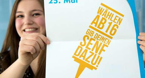 Eine Erstwählerin präsentiert ein Plakat des Landesjugendrings mit der Aufschrift: "Wählen ab 16. Gib Deinen Senf dazu". (Foto: dpa)