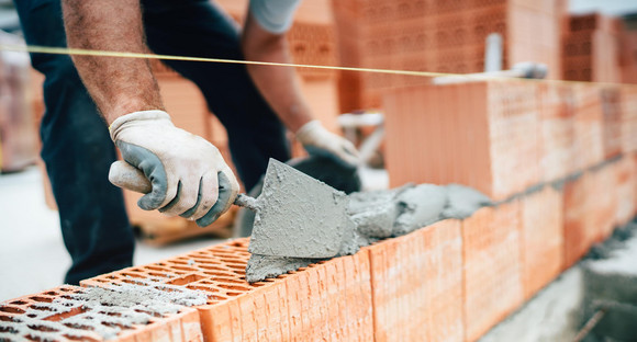 Ein Maurer arbeitet mit Zement und Mörtel an einer Ziegelwand.