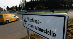 Ein Schild mit der Aufschrift &bdquo;Fl&uuml;chtlingserstaufnahmestelle&ldquo;, im Hintergrund ein Fahrzeug an einer Einfahrt.